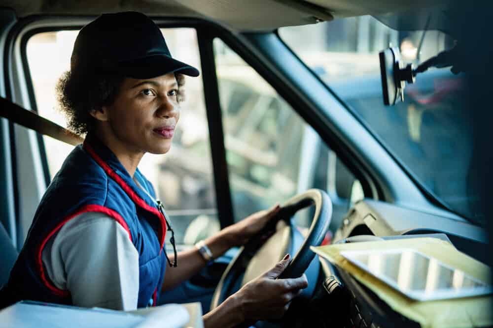 African American female courier driving delivery van in the city.