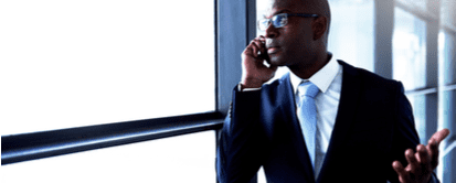 An upset businessman talking to someone on his mobile phone beside a window inside an office building.